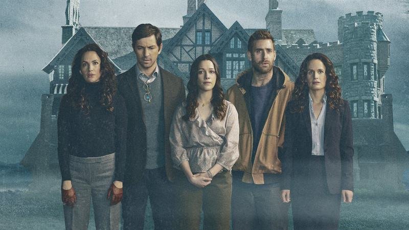 Cinco pessoas em pé, alinhadas diante de uma grande casa antiga de aparência sombria, com clima de névoa ao redor.