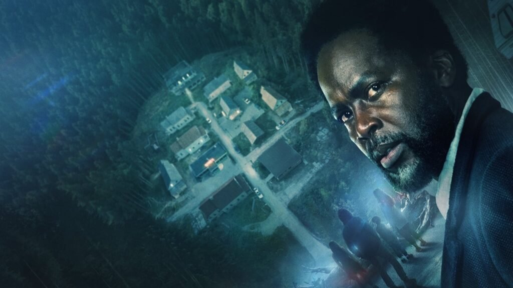 Poster de uma série de terror mostrando um homem sério em destaque à direita e, ao fundo, uma pequena cidade cercada por uma floresta densa, vista de cima.